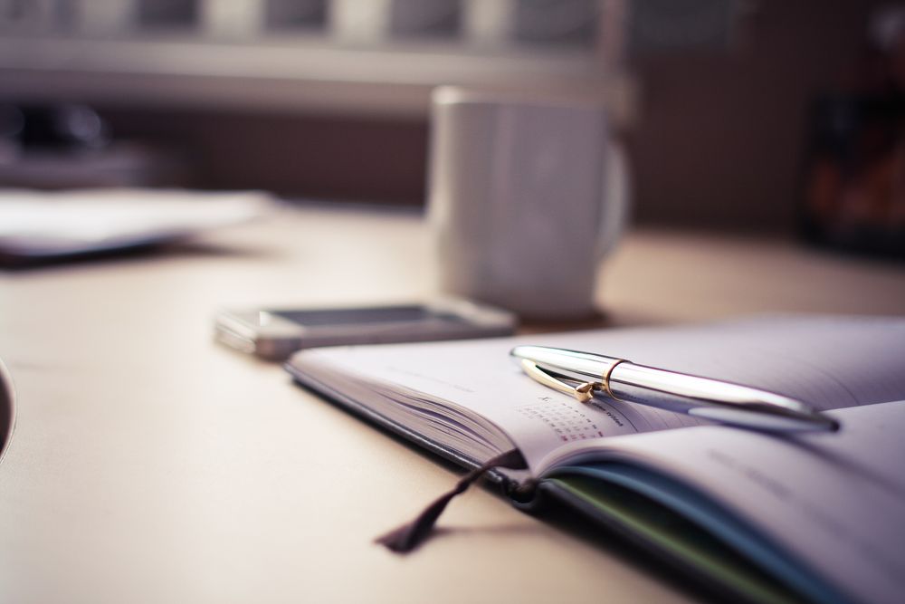 An open planner with a pen and a mug